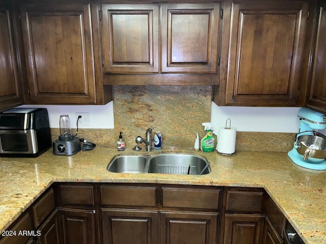 kitchen featuring dark brown cabinetry, sink, and light stone counters