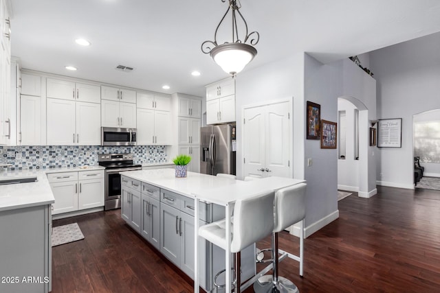 kitchen featuring white cabinets, decorative light fixtures, stainless steel appliances, tasteful backsplash, and a breakfast bar