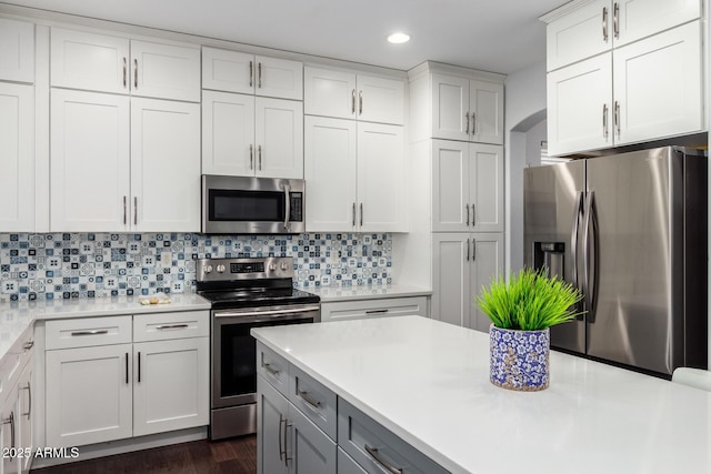 kitchen featuring white cabinets, backsplash, appliances with stainless steel finishes, and dark wood-type flooring