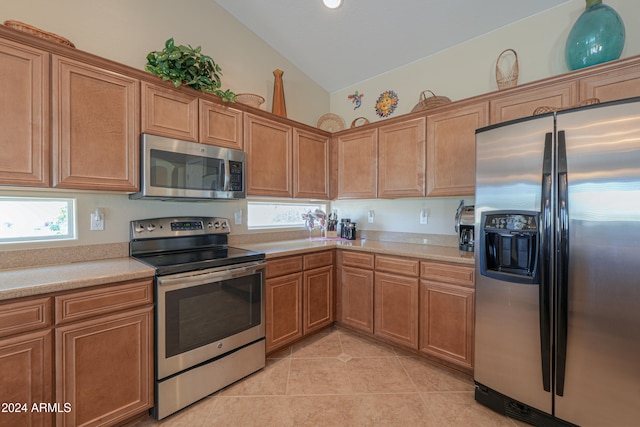 kitchen with light tile patterned flooring, vaulted ceiling, and appliances with stainless steel finishes