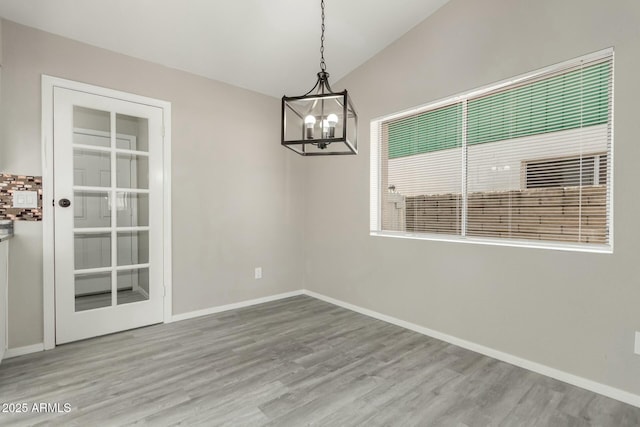 unfurnished dining area featuring lofted ceiling, a notable chandelier, and light hardwood / wood-style floors