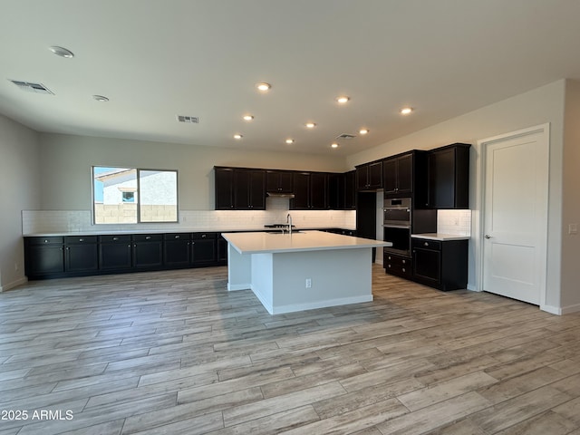17308 W Royal Palm Rd, Waddell, AZ 85355 - kitchen with decorative backsplash, light wood-style flooring, light countertops, recessed lighting, and a center island with sink