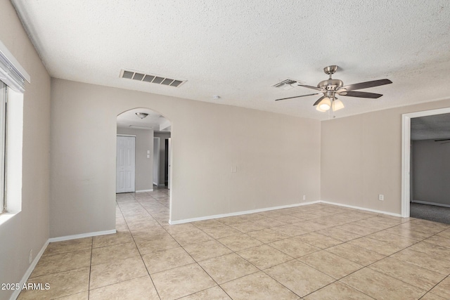 empty room with light tile patterned floors, arched walkways, a ceiling fan, and visible vents