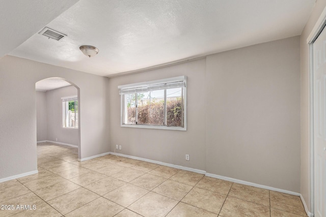 empty room with arched walkways, a textured ceiling, baseboards, light tile patterned floors, and visible vents