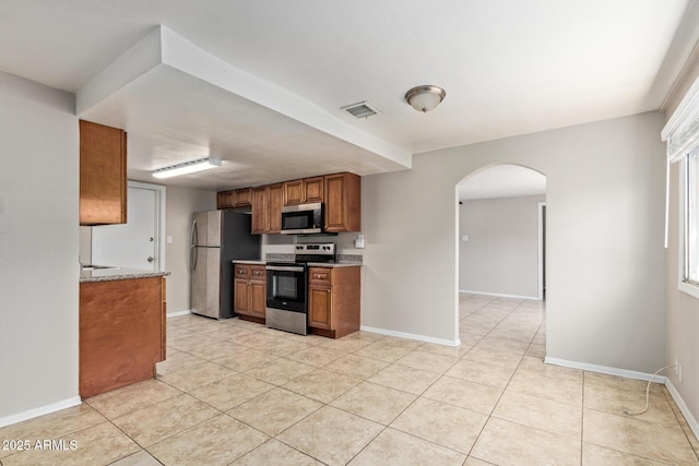 kitchen featuring brown cabinets, appliances with stainless steel finishes, arched walkways, baseboards, and light tile patterned floors
