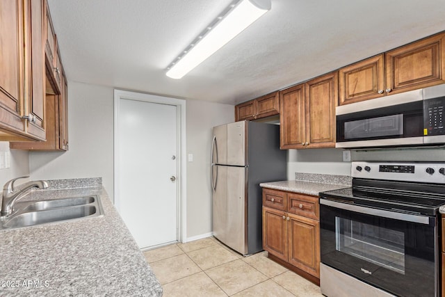 kitchen featuring light tile patterned flooring, appliances with stainless steel finishes, brown cabinetry, and a sink