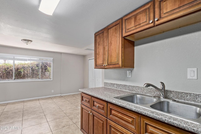 kitchen with a sink, light tile patterned flooring, and brown cabinets