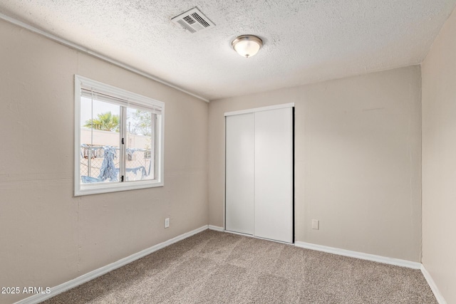 unfurnished bedroom with carpet flooring, a textured ceiling, baseboards, visible vents, and a closet