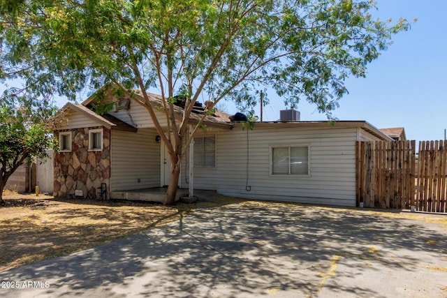 back of house with concrete driveway, fence, stone siding, and cooling unit