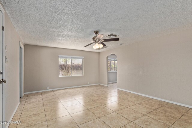 unfurnished room featuring ceiling fan, a textured ceiling, visible vents, arched walkways, and light tile patterned flooring