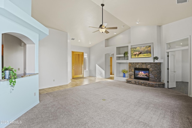 unfurnished living room with light carpet, a towering ceiling, ceiling fan, built in features, and a fireplace