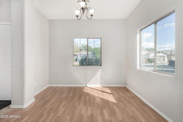 empty room with baseboards, an inviting chandelier, and light wood finished floors