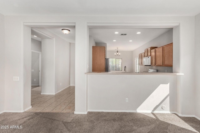 kitchen featuring an inviting chandelier, light tile patterned flooring, brown cabinetry, white microwave, and light colored carpet