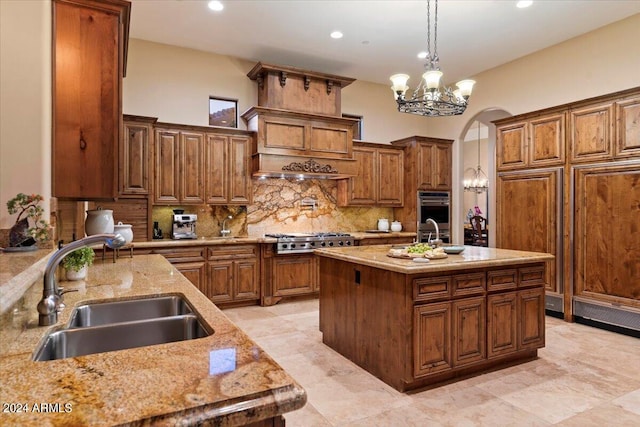 kitchen featuring appliances with stainless steel finishes, decorative light fixtures, an island with sink, sink, and a notable chandelier