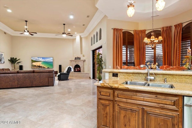 kitchen with light stone counters, ceiling fan with notable chandelier, sink, and hanging light fixtures