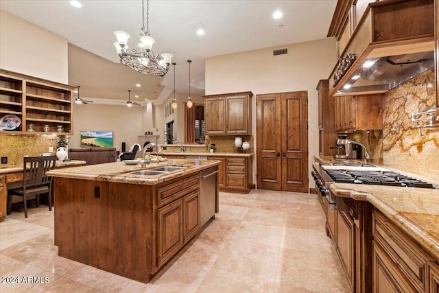 kitchen featuring a kitchen island with sink, sink, light stone countertops, and hanging light fixtures