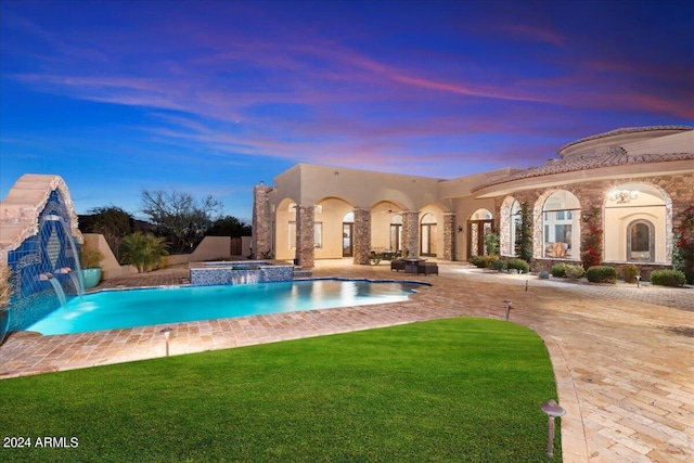 pool at dusk with an in ground hot tub, pool water feature, a patio, and a lawn