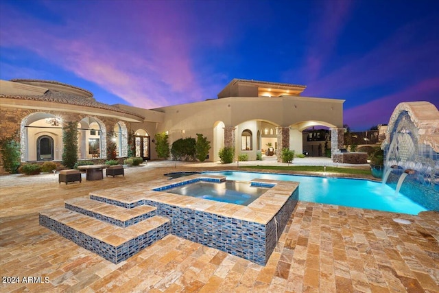 pool at dusk with a patio, pool water feature, and an in ground hot tub