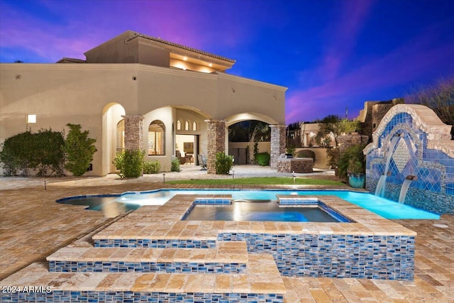 pool at dusk with an in ground hot tub, pool water feature, and a patio