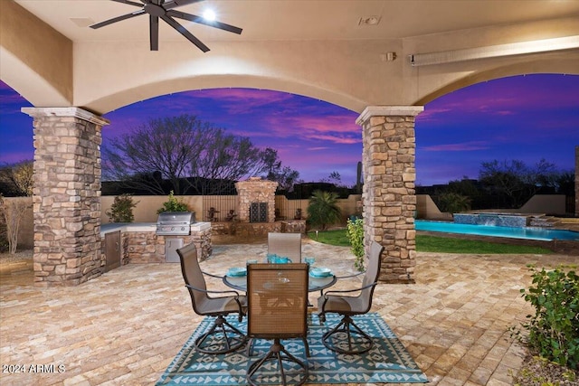 patio terrace at dusk with an outdoor fireplace, a grill, area for grilling, and ceiling fan