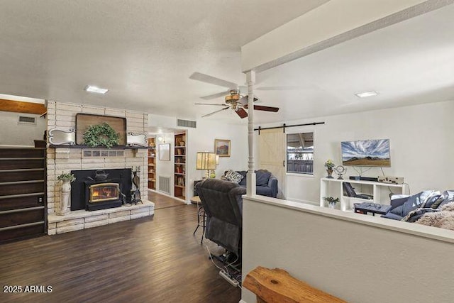 living area with a fireplace, visible vents, a barn door, a ceiling fan, and wood finished floors