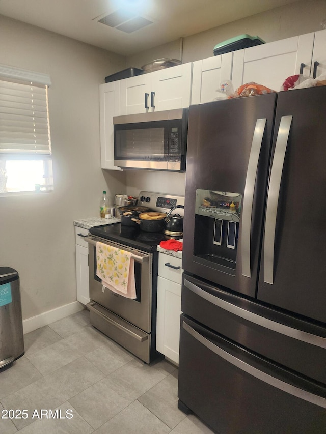 kitchen with appliances with stainless steel finishes, white cabinets, light countertops, light tile patterned floors, and baseboards