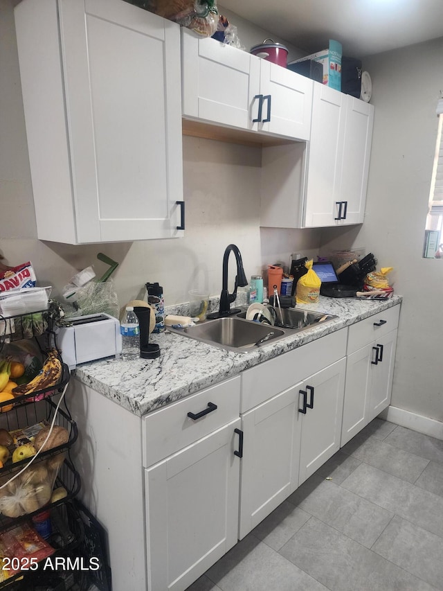 kitchen with baseboards, light stone countertops, a toaster, white cabinetry, and a sink