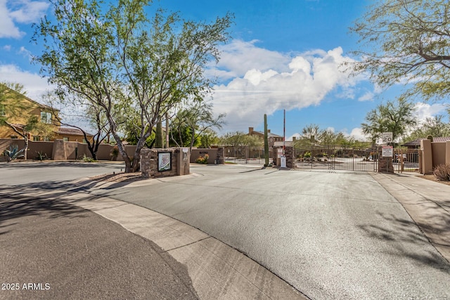 view of asphalt road with a gate, a gated entry, and sidewalks