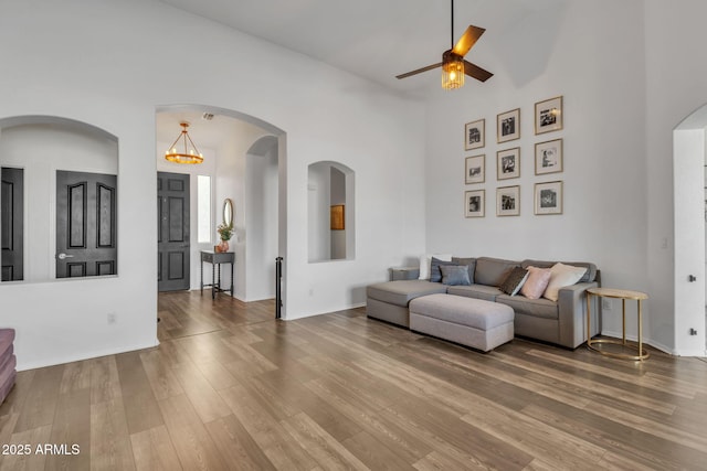 living room featuring hardwood / wood-style flooring, ceiling fan with notable chandelier, and a towering ceiling