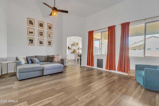 living room featuring a high ceiling, ceiling fan, and light wood-type flooring