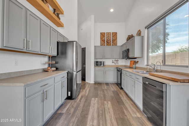 kitchen with sink, hardwood / wood-style flooring, gray cabinets, stainless steel appliances, and a high ceiling