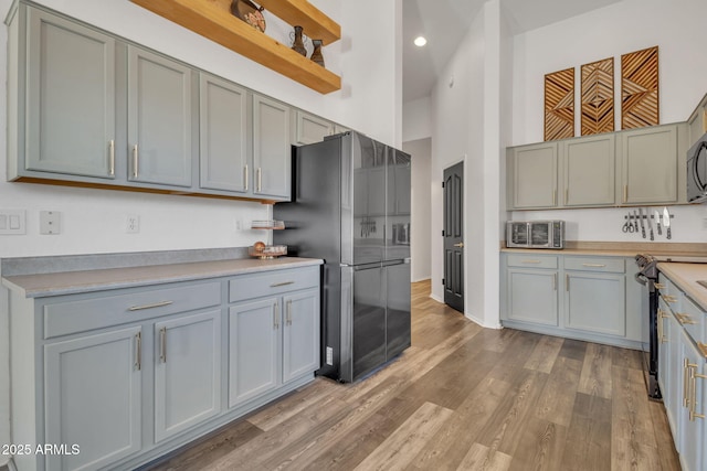 kitchen with gray cabinetry, stainless steel appliances, light hardwood / wood-style floors, and a high ceiling