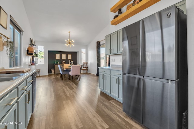 kitchen with lofted ceiling, appliances with stainless steel finishes, hardwood / wood-style floors, hanging light fixtures, and a notable chandelier