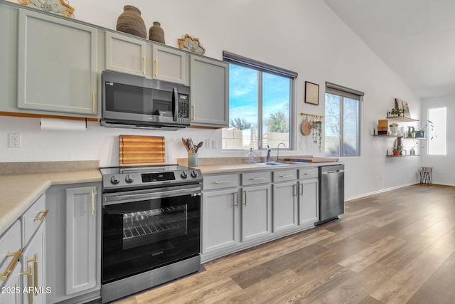 kitchen featuring vaulted ceiling, stainless steel appliances, sink, and light hardwood / wood-style flooring