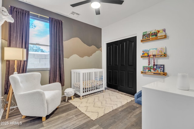 bedroom with a nursery area, ceiling fan, wood-type flooring, and a closet