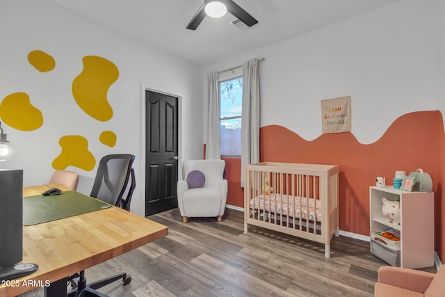 bedroom featuring ceiling fan, wood-type flooring, and a crib