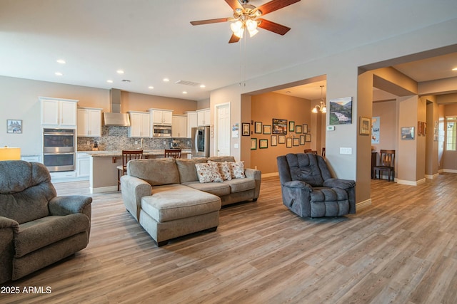 living room with ceiling fan with notable chandelier and light hardwood / wood-style floors