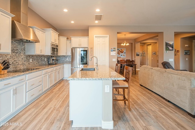 kitchen with sink, stainless steel fridge, an island with sink, black electric stovetop, and white cabinets