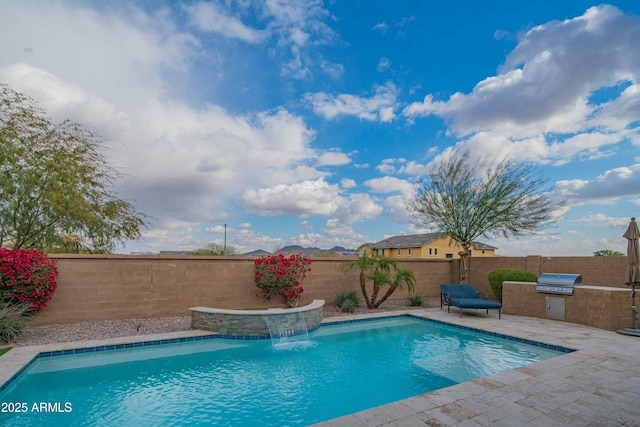 view of swimming pool with an outdoor kitchen, a grill, pool water feature, and a patio area