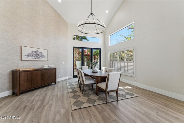 dining space with high vaulted ceiling, baseboards, a notable chandelier, and light wood finished floors