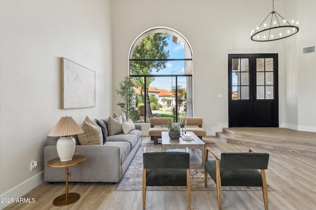 living room featuring light wood-type flooring, a notable chandelier, a towering ceiling, and baseboards