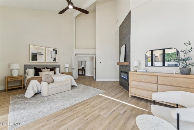 bedroom with wood finished floors, a ceiling fan, a towering ceiling, baseboards, and a tiled fireplace