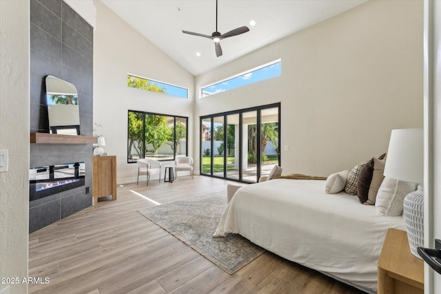 bedroom featuring access to outside, a high ceiling, light wood-style floors, a fireplace, and recessed lighting