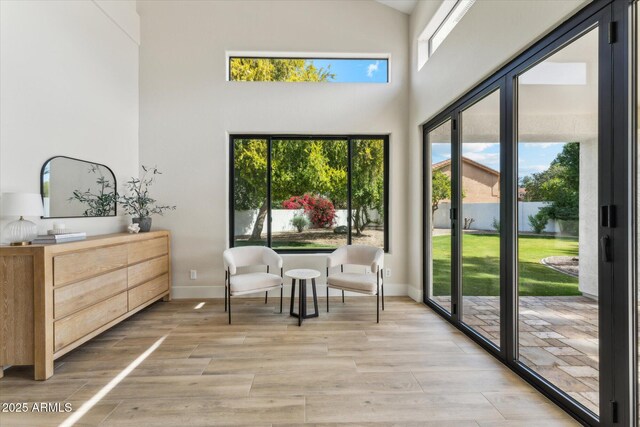 living area featuring a high ceiling, light wood-style flooring, and baseboards