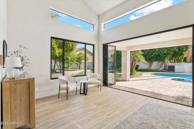 doorway featuring high vaulted ceiling, light wood-style flooring, and baseboards