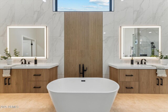 full bathroom with a freestanding bath, two vanities, a sink, and tile walls