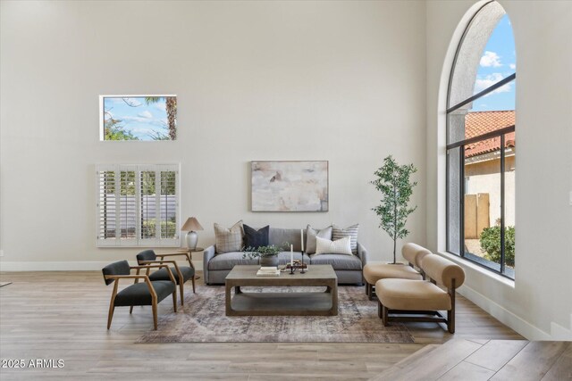 living area with light wood-type flooring, plenty of natural light, a high ceiling, and baseboards