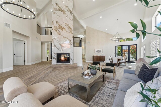 living area with a fireplace, visible vents, light wood-type flooring, beamed ceiling, and an inviting chandelier