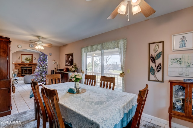 dining space with light tile patterned floors, a brick fireplace, and ceiling fan