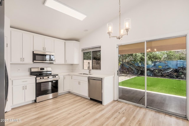 kitchen with appliances with stainless steel finishes, a sink, light countertops, white cabinets, and lofted ceiling